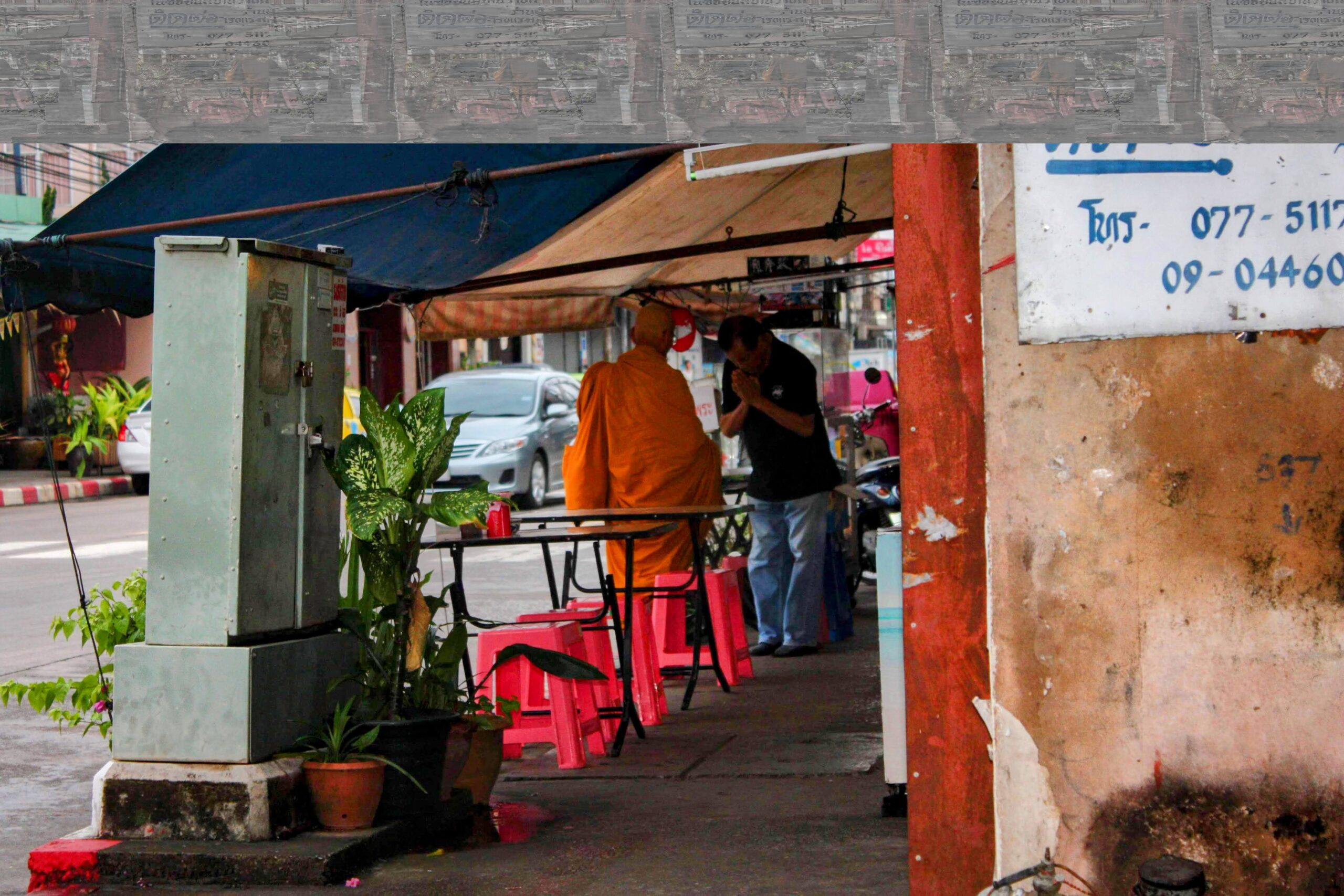 Thai man making the Wai gesture to a monk in a simple restaurant in Chumphon, Thailand, during an early morning interaction.