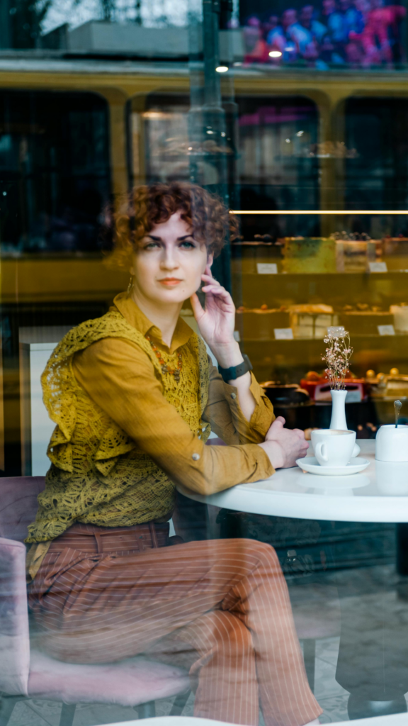 An international woman sitting in a café, reflecting quietly while navigating integration with self-respect in a new cultural environment.
