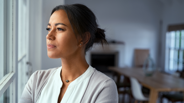 A woman reflecting calmly by a window, navigating life in a new cultural environment with integration and self-respect.